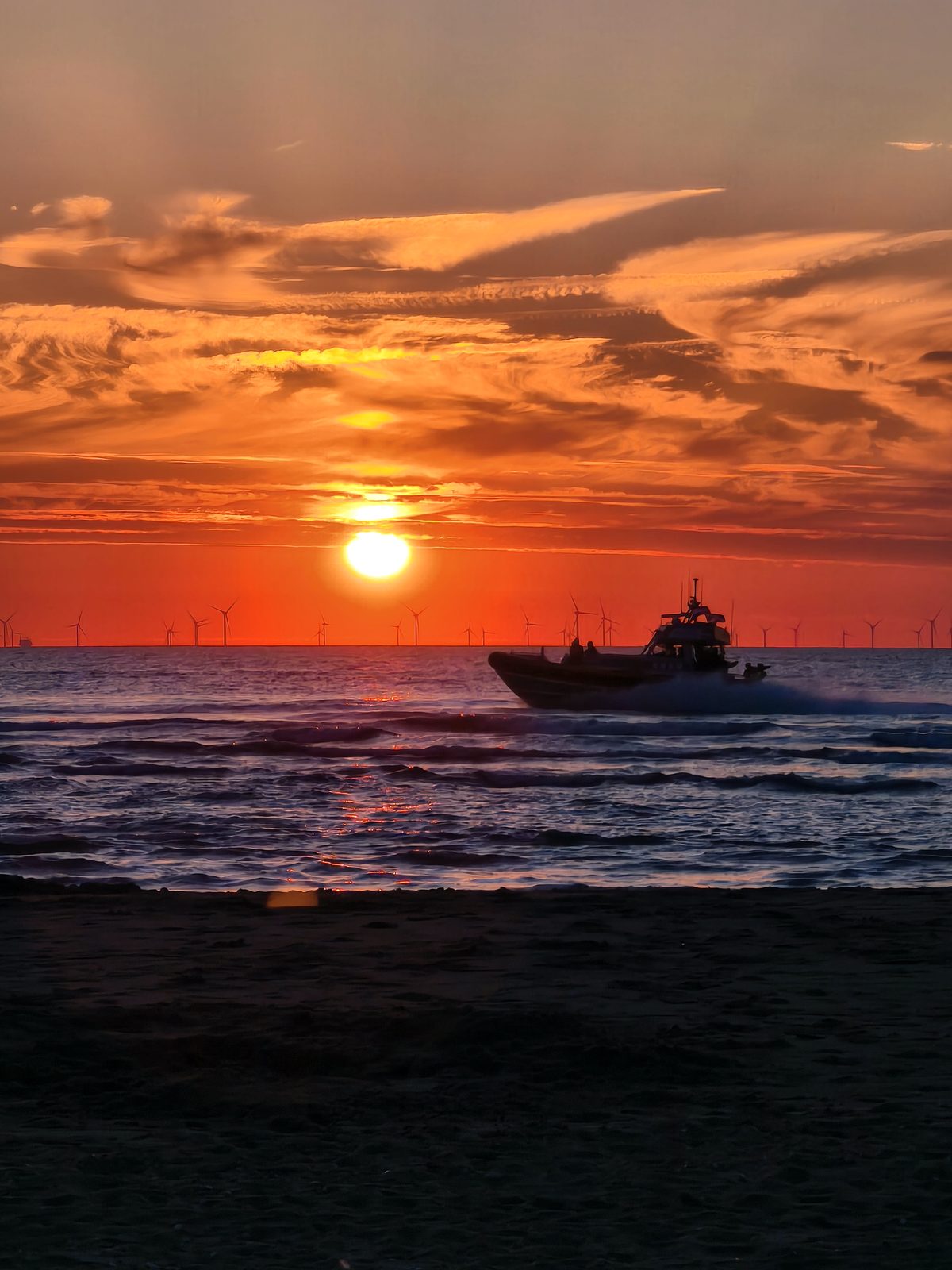 Schnellboot vor goldenem Sonnenuntergang über dem Meer mit Offshore-Windkraftanlagen am Horizont