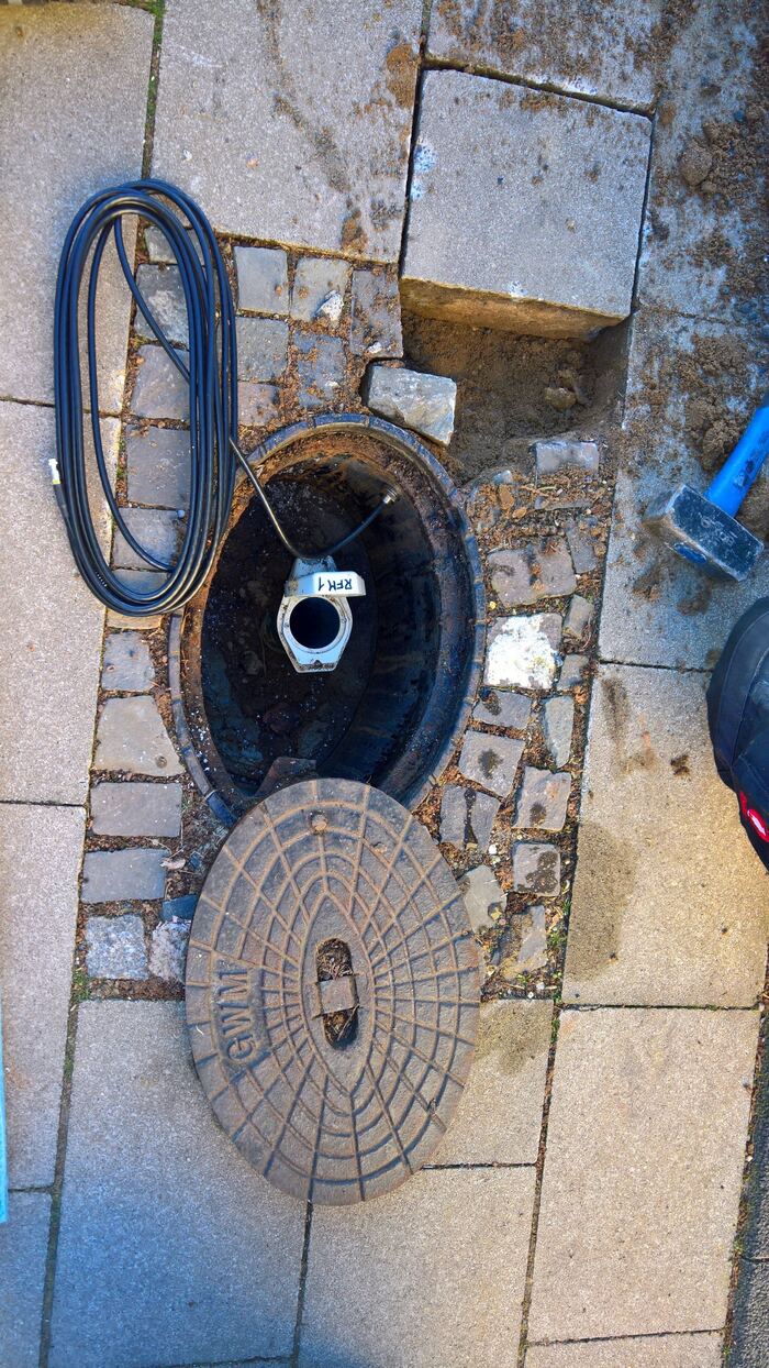Grundwasser-Messstelle im öffentlichen Gehweg: Pegelrohr und Logger bündig eingebaut, unauffällig, aber stündlich aktiv.