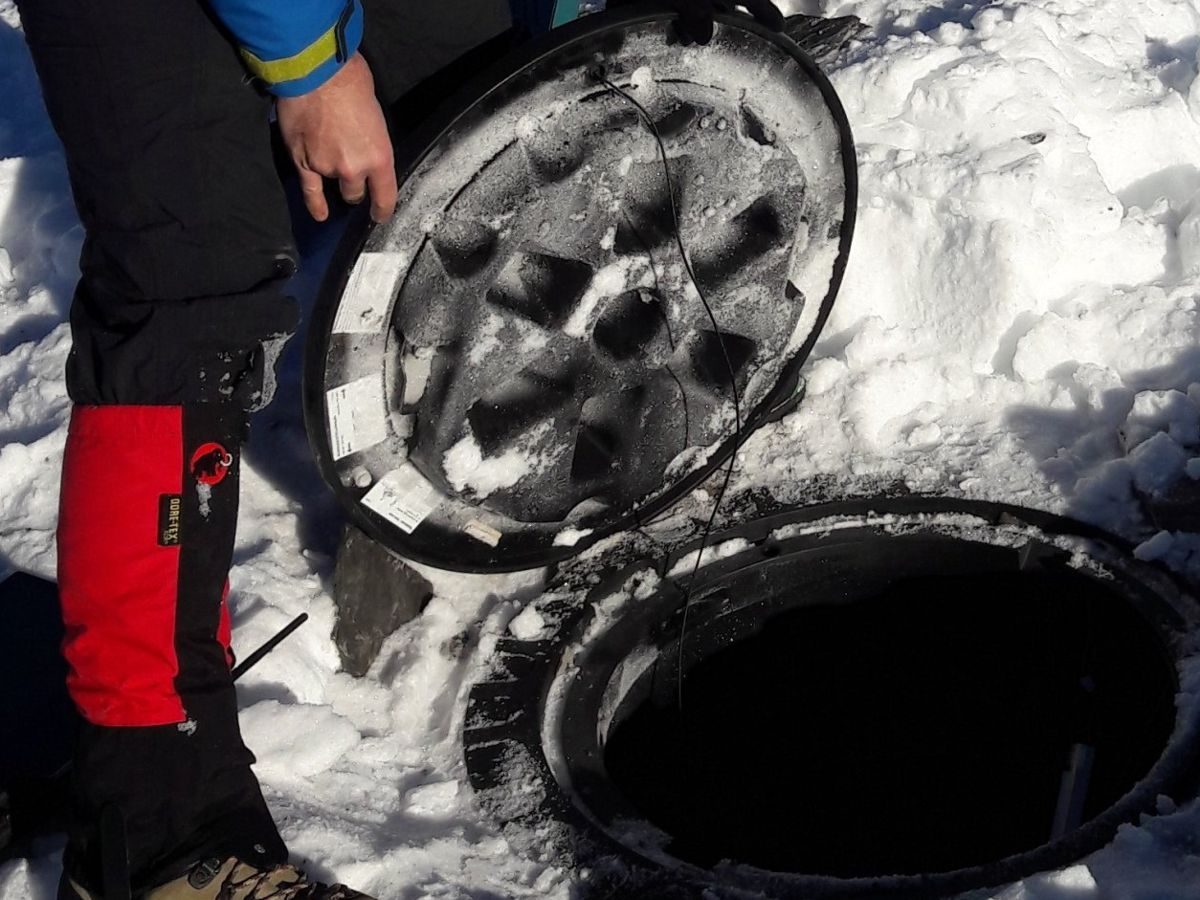 Techniker hebt im Schnee einen Schachtdeckel an, Temperatur-Messkette wird herausgeführt