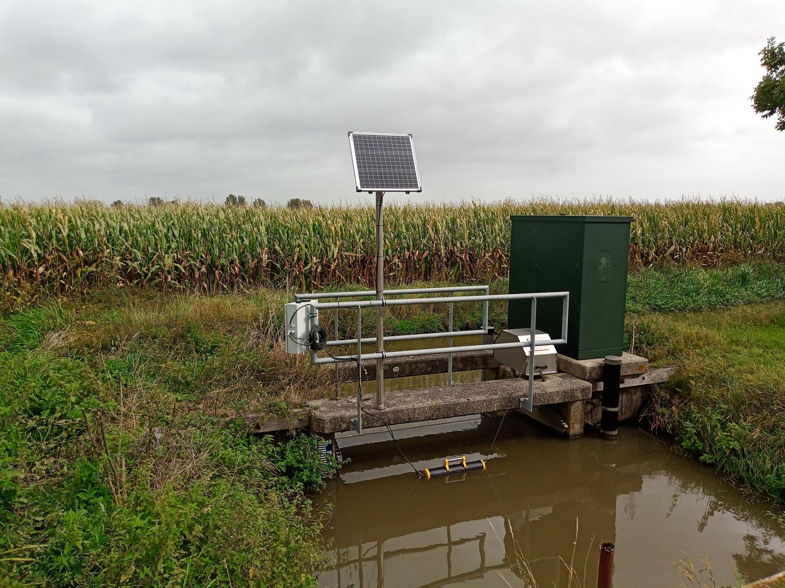Pegelstation am Wehr mit Solarpanel zwischen Maisfeldern, robuster Außenbereich